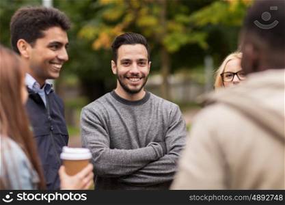 people, friendship, communication and international concept - group of happy friends walking along autumn park and drinking coffee