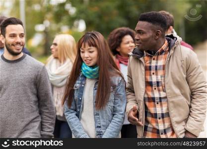 people, friendship, communication and international concept - group of happy friends walking along autumn park