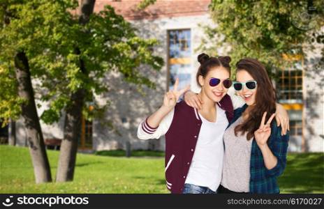 people, friendship, fashion, education and teens concept - happy smiling pretty teenage girls in sunglasses showing peace hand sign ver summer campus background
