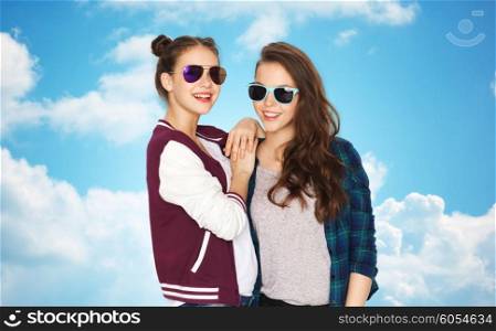 people, friendship, fashion, summer and teens concept - happy smiling pretty teenage girls in sunglasses over blue sky and clouds background