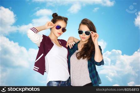people, friendship, fashion, summer and teens concept - happy smiling pretty teenage girls in sunglasses over blue sky and clouds background