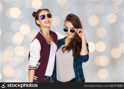people, friendship, fashion, summer and teens concept - happy smiling pretty teenage girls in sunglasses over holidays lights background