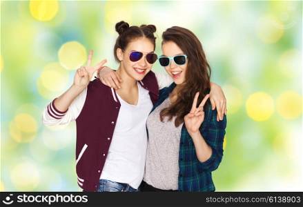 people, friendship, fashion, summer and teens concept - happy smiling pretty teenage girls in sunglasses showing peace hand sign over green holidays lights background