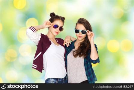 people, friendship, fashion, summer and teens concept - happy smiling pretty teenage girls in sunglasses over green holidays lights background