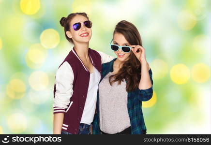 people, friendship, fashion, summer and teens concept - happy smiling pretty teenage girls in sunglasses over green holidays lights background