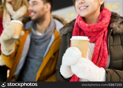 people, friendship, hot drinks and leisure concept - close up of happy friends drinking from paper coffee cups on skating rink