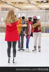 people, friendship, technology and leisure concept - friends wearing face protective masks for protection from virus disease taking photo with smartphone on skating rink. friends in masks taking photo on skating rink