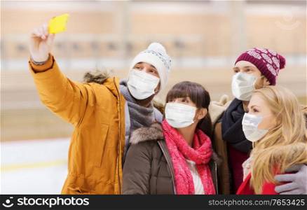 people, friendship, technology and leisure concept - friends wearing face protective medical masks for protection from virus disease taking selfie with smartphone on skating rink. friends in masks taking selfie on skating rink
