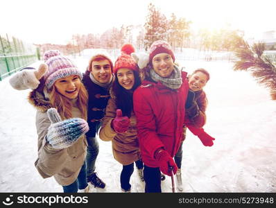 people, friendship, technology and leisure concept - happy friends taking picture with smartphone selfie stick and showing thumbs up on ice skating rink outdoors. happy friends with smartphone on ice skating rink