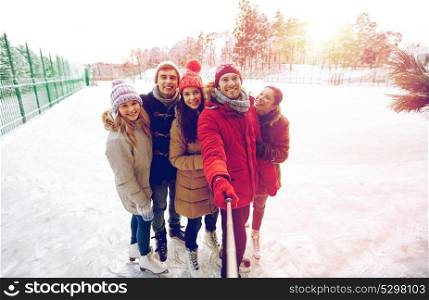 people, friendship, technology and leisure concept - happy friends taking picture with smartphone selfie stick on ice skating rink outdoors. happy friends with smartphone on ice skating rink