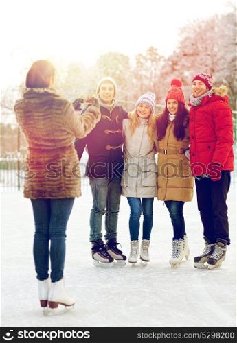 people, friendship, technology and leisure concept - happy friends taking picture with smartphone on ice skating rink outdoors. happy friends with smartphone on ice skating rink