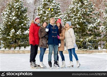 people, friendship, technology and leisure concept - happy friends taking picture with smartphone selfie stick on ice skating rink outdoors