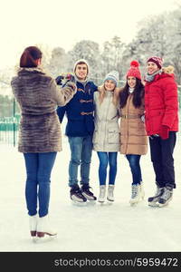 people, friendship, technology and leisure concept - happy friends taking picture with smartphone on ice skating rink outdoors