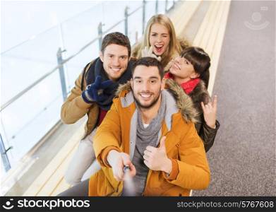 people, friendship, technology and leisure concept - happy friends taking selfie with camera or smartphone and selfie stick on skating rink