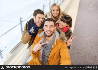 people, friendship, technology and leisure concept - happy friends taking selfie with camera or smartphone on skating rink