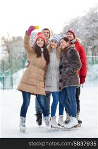 people, friendship, technology and leisure concept - happy friends taking selfie with smartphone on ice skating rink outdoors