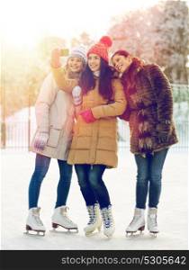 people, friendship, technology and leisure concept - happy girl friends taking selfie with smartphone on ice skating rink outdoors. happy young women with smartphone on skating rink