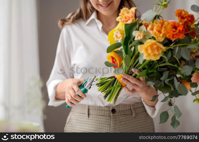 people, gardening and floral design concept - close up of happy smiling woman or floral artist making bunch of flowers and cutting stems with pruning shears at home. happy woman making bunch of flowers at studio