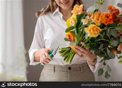 people, gardening and floral design concept - close up of happy smiling woman or floral artist making bunch of flowers and cutting stems with pruning shears at home. happy woman making bunch of flowers at studio