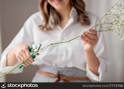 people, gardening and floral design concept - close up of happy smiling woman or floral artist cutting gypsophila stem with pruning shears at home. woman cutting flower stem with pruning shears