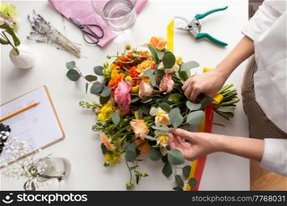 people, gardening and floral design concept - close up of woman or floral artist making bunch of flowers and tying bow on table at studio. woman or floral artist making bunch of flowers