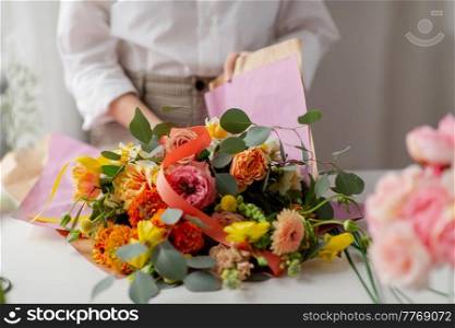 people, gardening and floral design concept - close up of woman or floral artist wrapping flowers to craft paper at studio. woman wrapping flowers to craft paper at studio