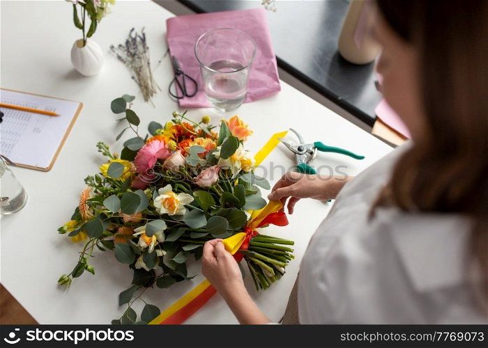 people, gardening and floral design concept - close up of woman or floral artist making bunch of flowers and tying bow on table at studio. woman or floral artist making bunch of flowers