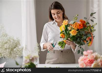 people, gardening and floral design concept - happy smiling woman or floral artist making bunch of flowers and cutting stems with pruning shears at home. happy woman making bunch of flowers at home