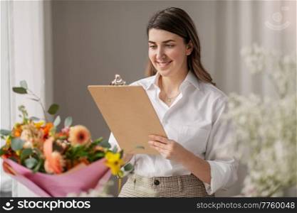 people, gardening and floral design concept - happy smiling woman or floral artist with clipboard and flowers working at studio. happy woman with clipboard and flowers at studio