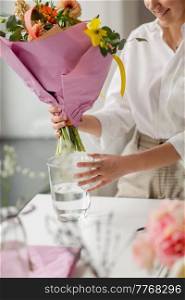 people, gardening and floral design concept - happy smiling woman or floral artist with bunch of flowers and vase working at studio. happy woman or floral artist with flowers at home
