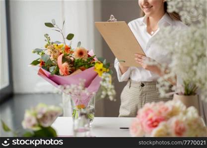 people, gardening and floral design concept - happy smiling woman or floral artist with clipboard and flowers working at studio. happy woman with clipboard and flowers at studio