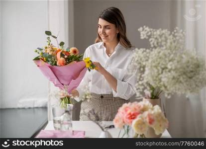 people, gardening and floral design concept - happy woman or floral artist arranging flowers in vase at home. happy woman arranging flowers in vase at home