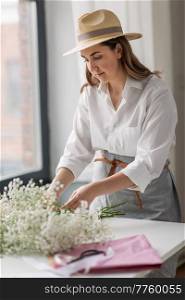 people, gardening and floral design concept - happy woman or floral artist in straw hat with bunch of gypsophila flowers working at studio. happy woman with gypsophila flowers at studio