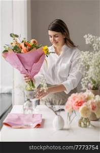 people, gardening and floral design concept - happy woman or floral artist putting bunch of flowers in vase at home. happy woman arranging flowers in vase at home