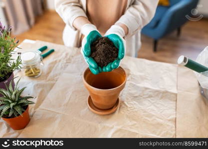 people, gardening and housework concept - close up of woman in gloves pouring soil to flower pot at home. close up of woman planting pot flowers at home