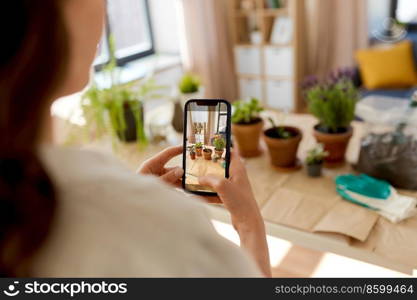 people, gardening and housework concept - close up of woman with smartphone photographing pot flowers at home. woman with smartphone photographing pot flowers