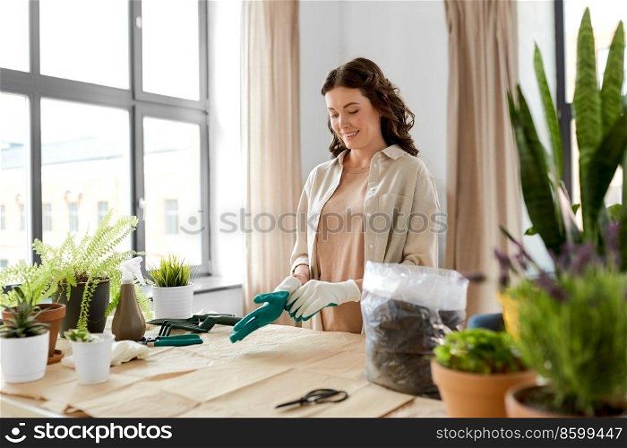 people, gardening and housework concept - happy smiling woman wearing gloves for planting flowers at home. happy woman with gloves planting flowers at home