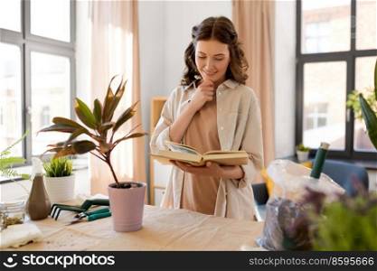 people, gardening and housework concept - happy smiling woman with book planting pot flowers at home. happy woman with book planting pot flowers at home