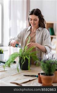 people, gardening and housework concept - happy woman cutting fern flower’s leaves with pruner at home. woman cutting flower’s leaves with pruner at home