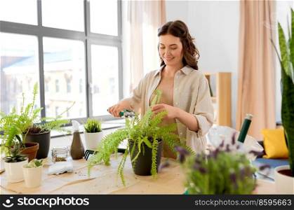 people, gardening and housework concept - happy woman cutting fern flower’s leaves with pruner at home. woman cutting flower’s leaves with pruner at home