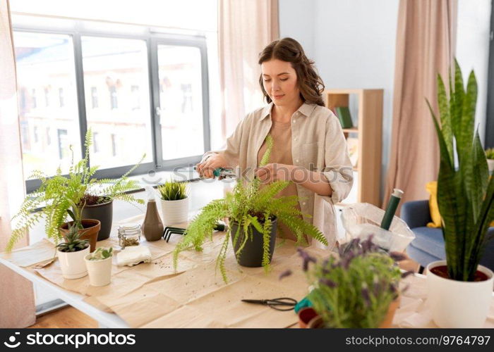 people, gardening and housework concept - happy woman cutting fern flower’s leaves with pruner at home. woman cutting flower’s leaves with pruner at home