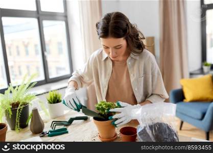 people, gardening and housework concept - happy woman in gloves planting pot flowers at home. happy woman planting pot flowers at home