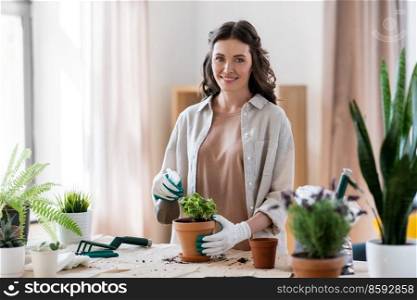people, gardening and housework concept - happy woman in gloves with spray planting pot flowers at home. happy woman planting pot flowers at home
