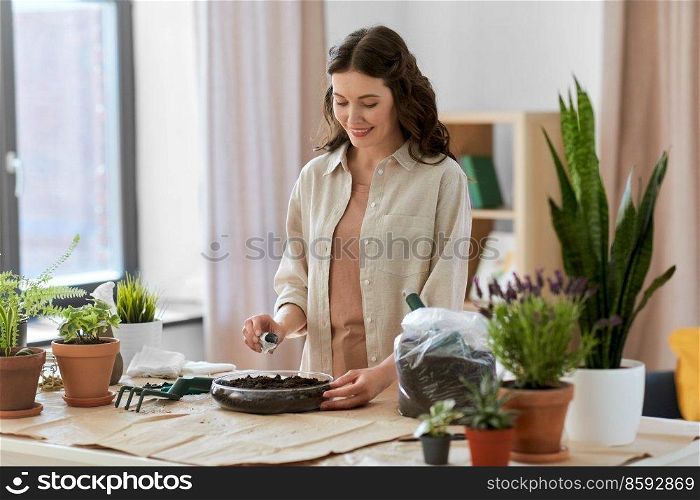people, gardening and housework concept - happy woman pouring seeds to soil in glass vase and planting flowers at home. happy woman planting pot flowers at home
