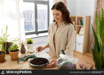 people, gardening and housework concept - happy woman pouring seeds to soil in glass vase and planting flowers at home. happy woman planting pot flowers at home