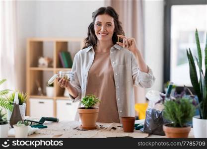 people, gardening and housework concept - happy woman with fertilizing spikes in jar planting pot flowers at home. woman planting and fertilizing flowers at home