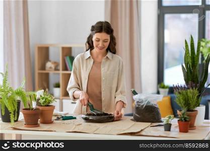 people, gardening and housework concept - happy woman with fork loosening soil in glass vase and planting flowers at home. happy woman planting pot flowers at home