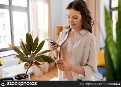 people, gardening and housework concept - happy woman with smartphone and pot flower at home. woman with smartphone and pot flower at home