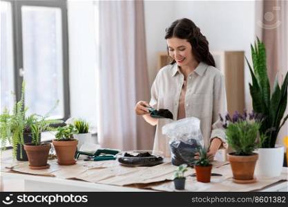 people, gardening and housework concept - happy woman with trowel and soil in bag planting flowers in glass vase at home. happy woman planting pot flowers at home