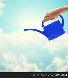people, gardening and profession concept - close up of woman or gardener hand holding watering can over blue sky with clouds